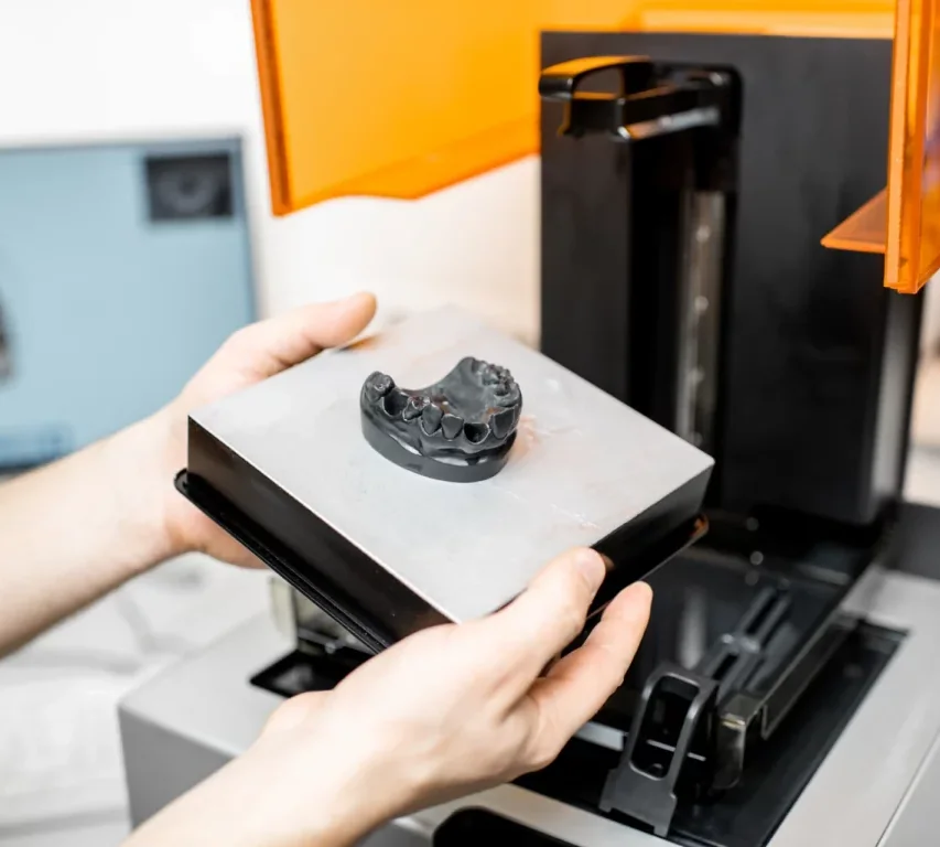 A technician lifting a printed jaw model out of a 3D printer