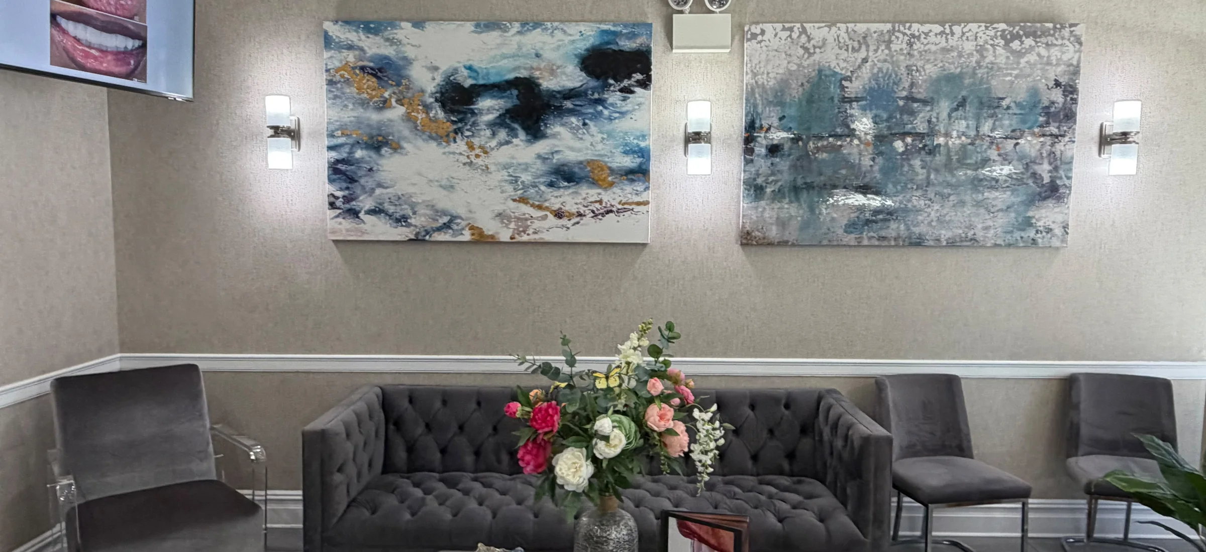 The lounge of the waiting area, with grey sofas, flowers and blue abstract paintings