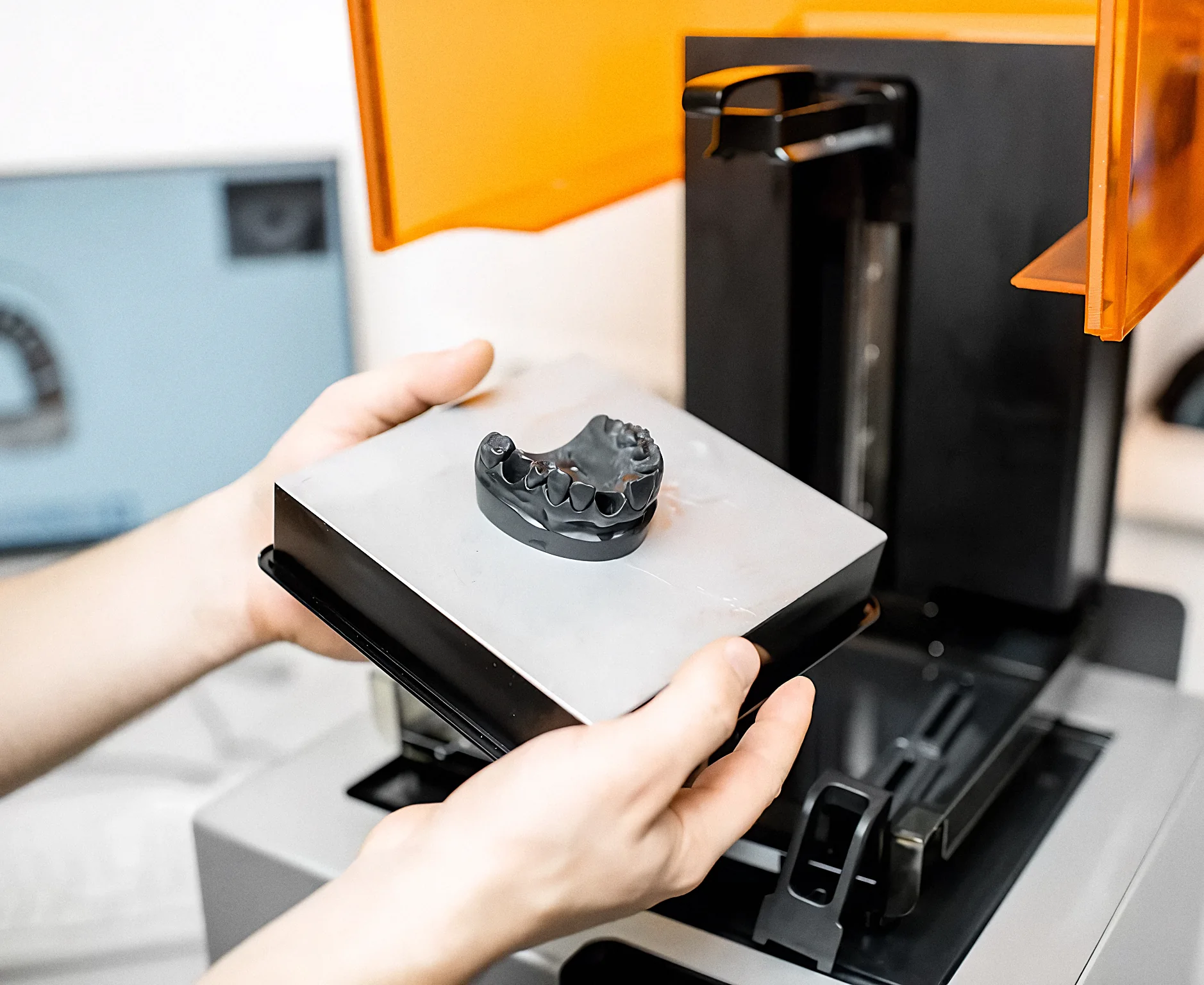 A technician lifting a printed jaw model out of a 3D printer