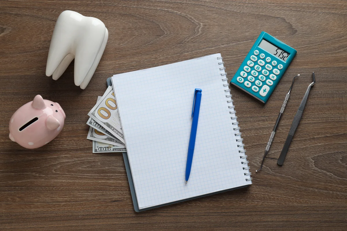 A tooth model, a piggy bank, a calculator and a notebook on a wooden desk