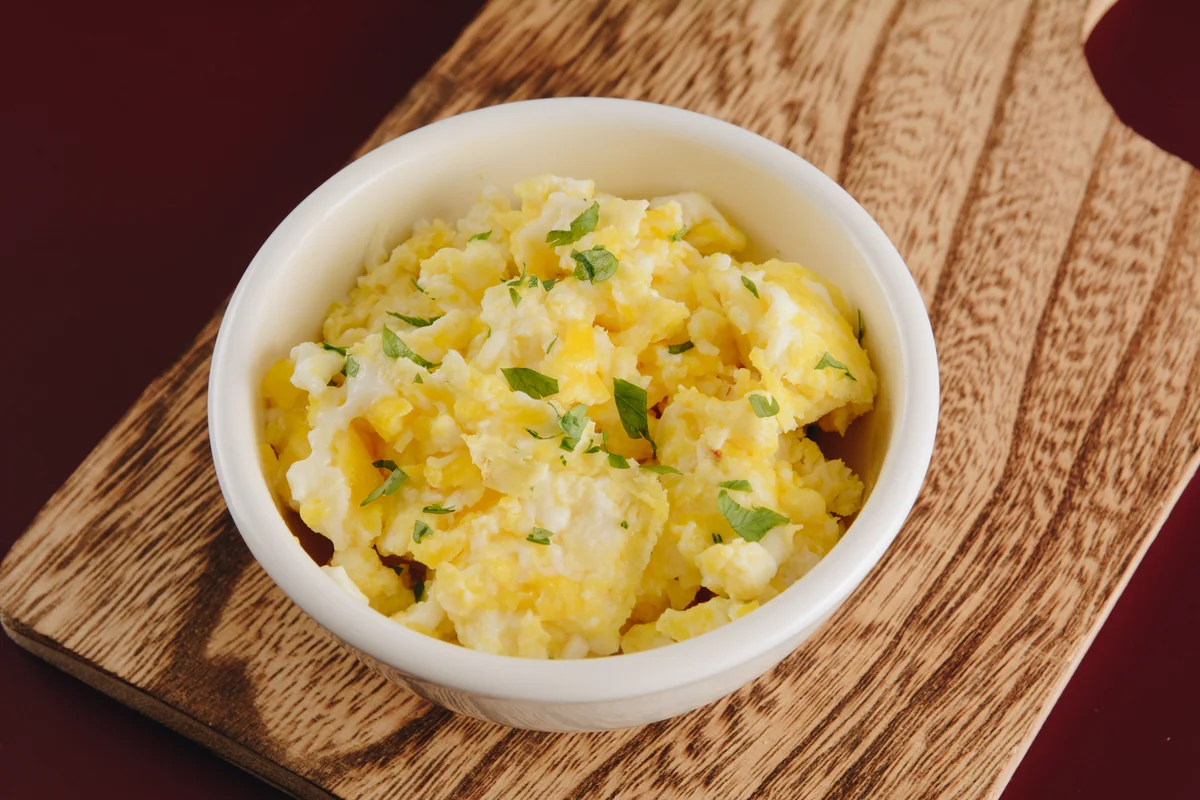 A bowl of soft scrambled eggs on a wooden board