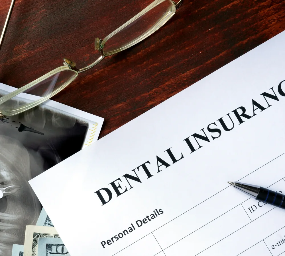 A dental insurance form with a pen, reading glasses, an X-ray and dollar bills