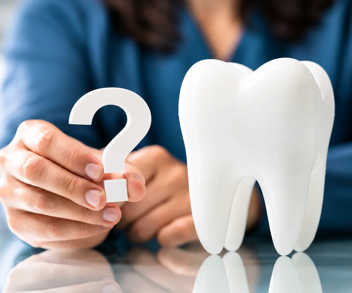 A patient holding a question mark beside a large model tooth