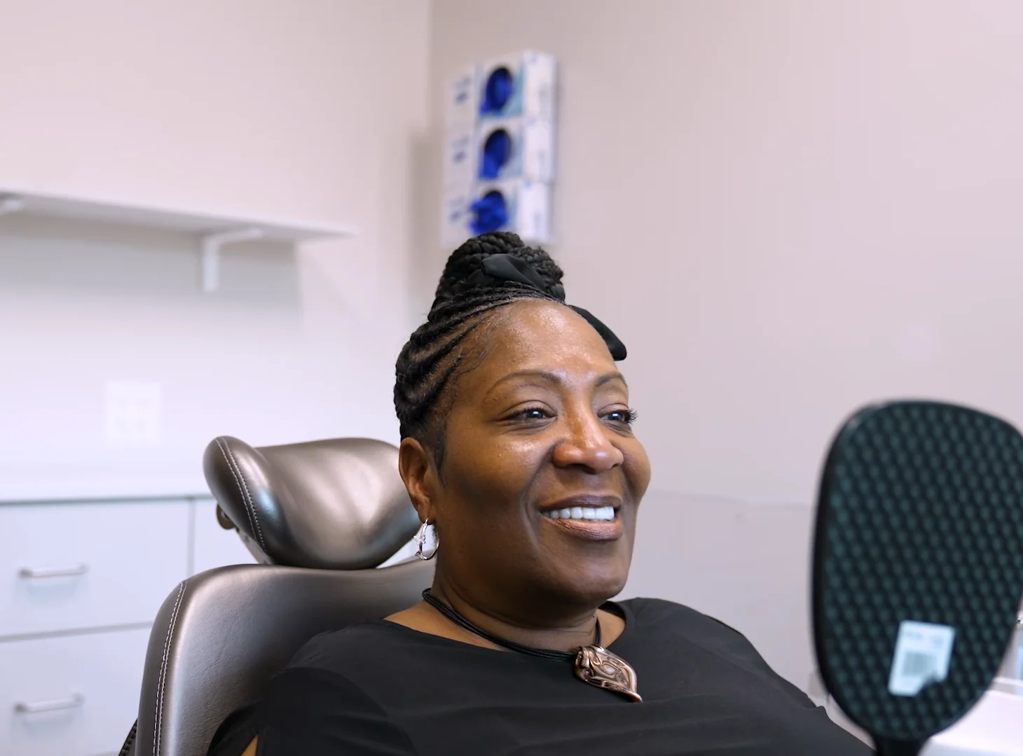 A patient smiling at her new teeth in a hand mirror in the treatment chair