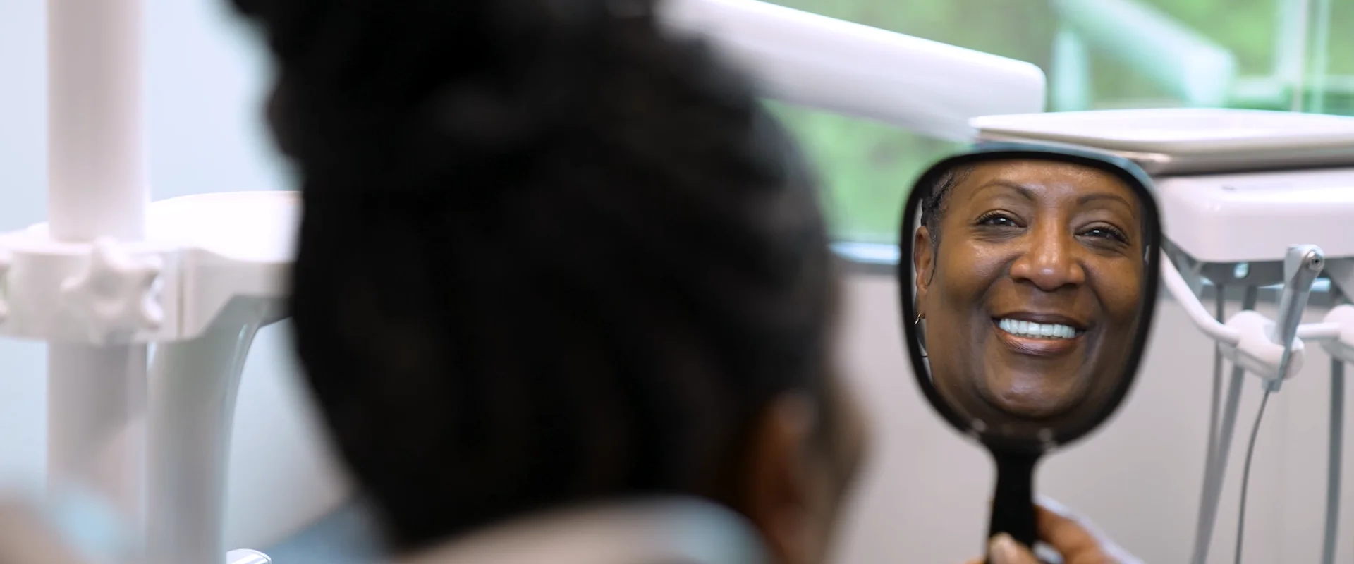 A patient sees her new smile in a hand mirror in the treatment chair