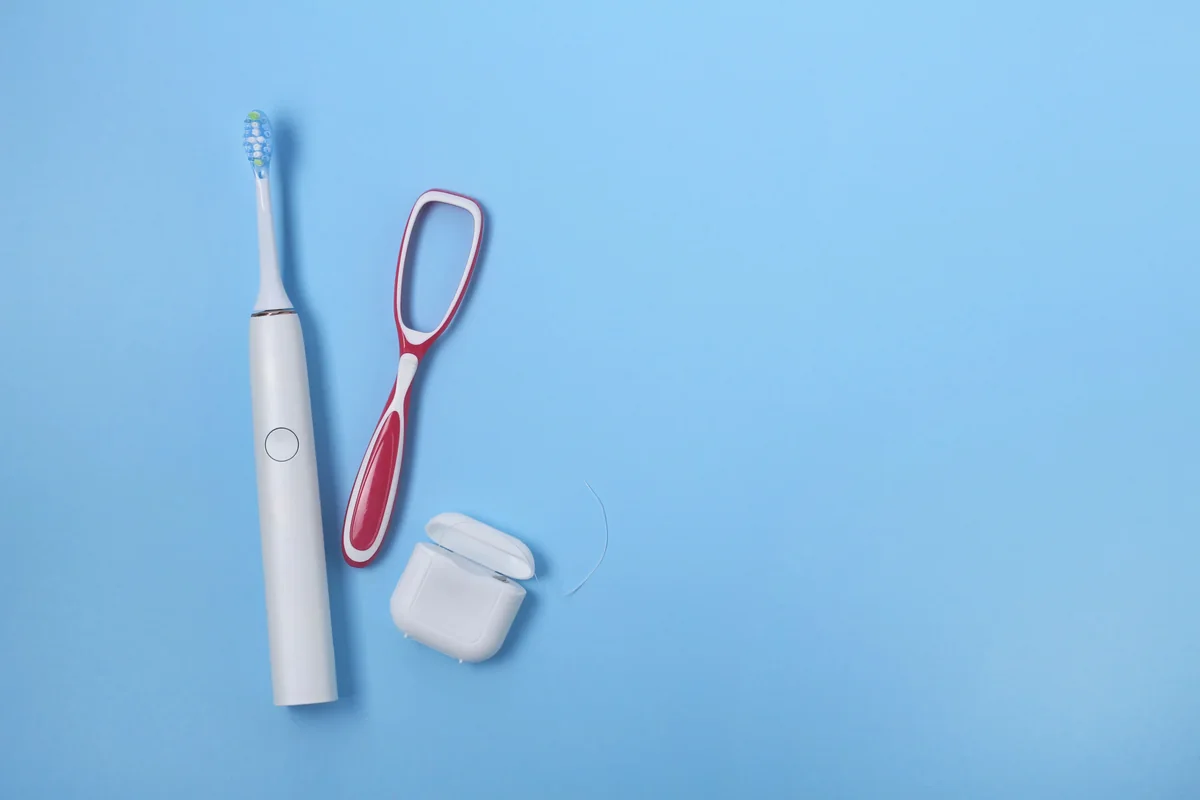 An electric toothbrush, a tongue scraper and dental floss on a blue background