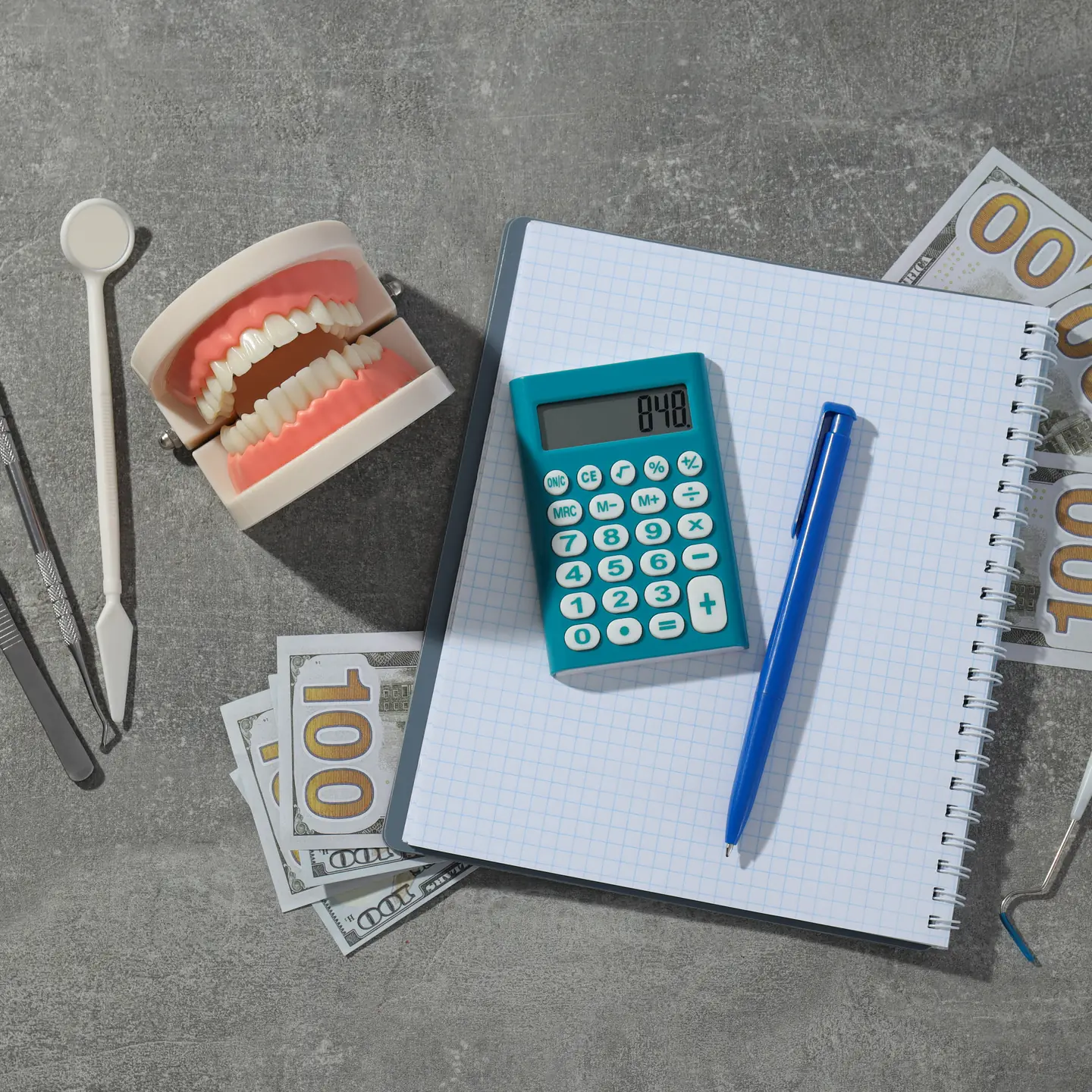 A tooth model, a calculator, a notebook and dental instruments