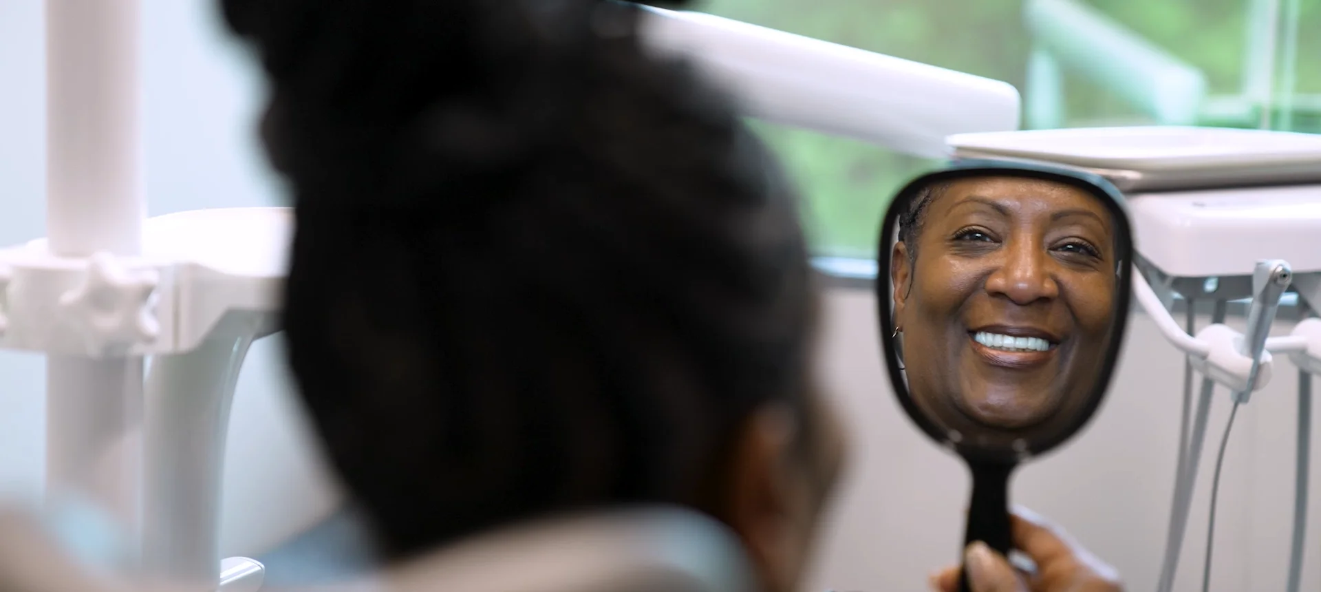 A patient sees her new smile in a hand mirror in the treatment chair