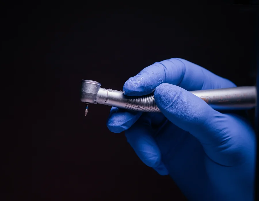 A gloved hand holding a dental handpiece