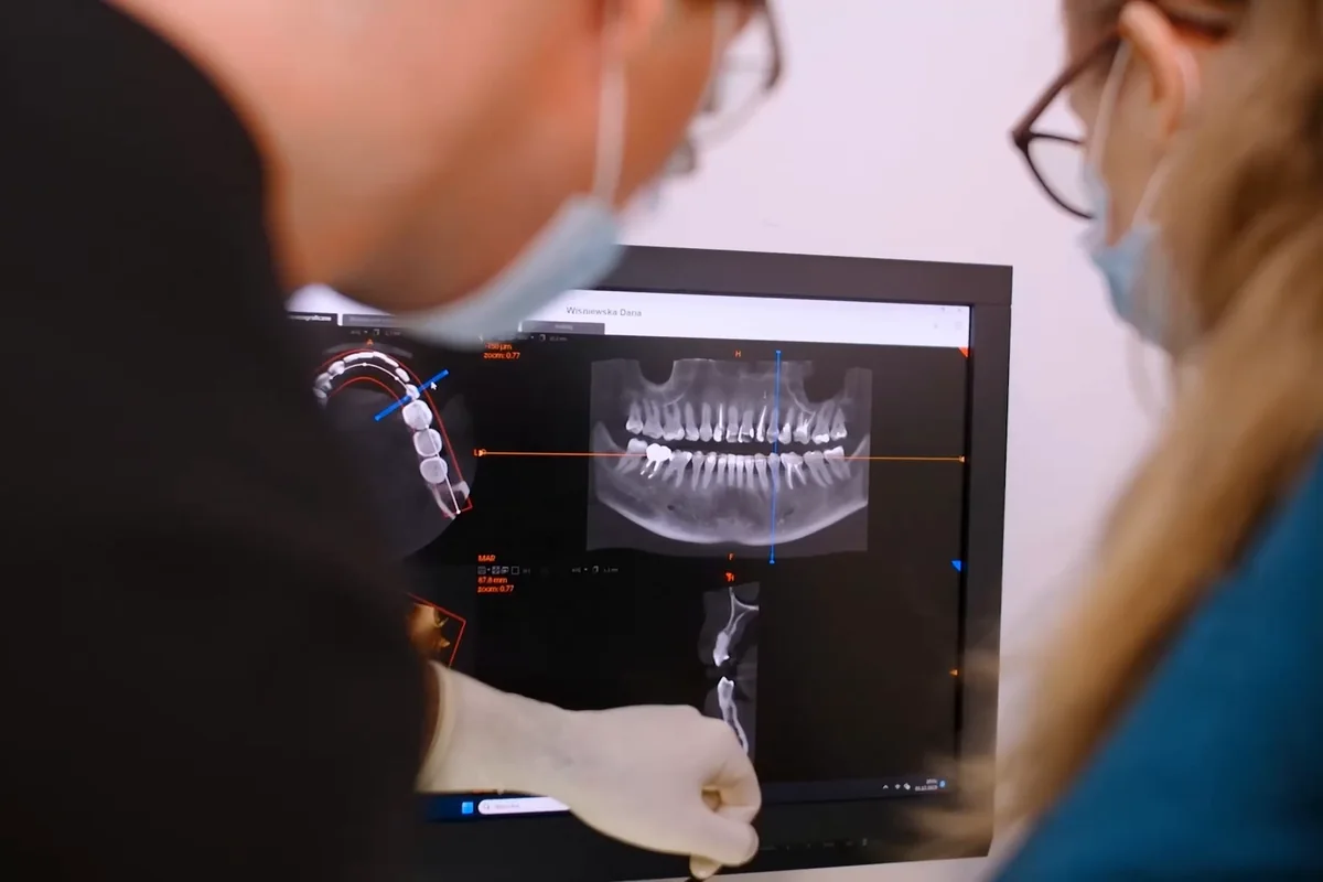 A dentist and an assistant reviewing a panoramic scan on the treatment-room screen