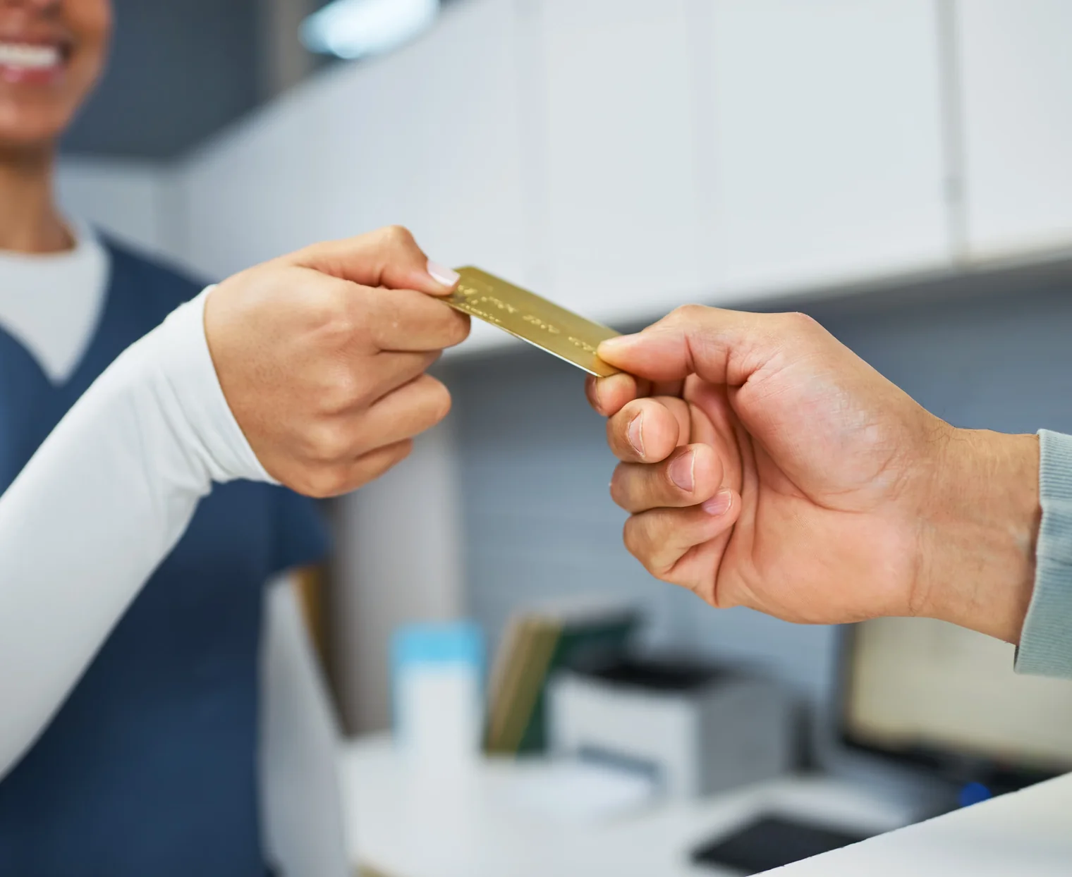 A patient handing a payment card across the front desk to a smiling team member