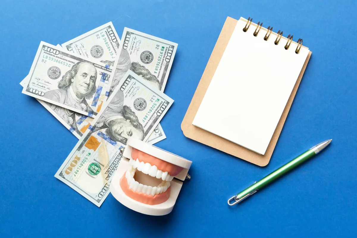 A model of teeth beside dollar bills, a notepad and a pen