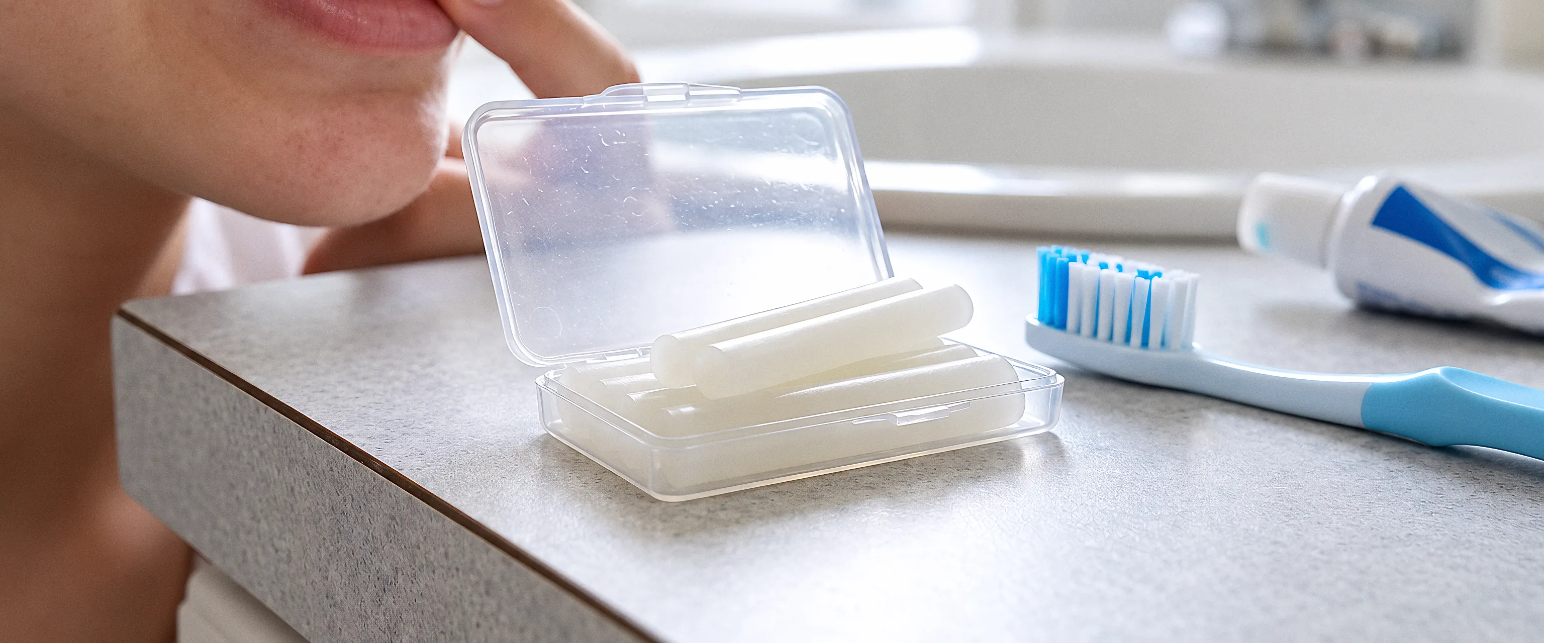 Orthodontic wax in its case beside a toothbrush and toothpaste