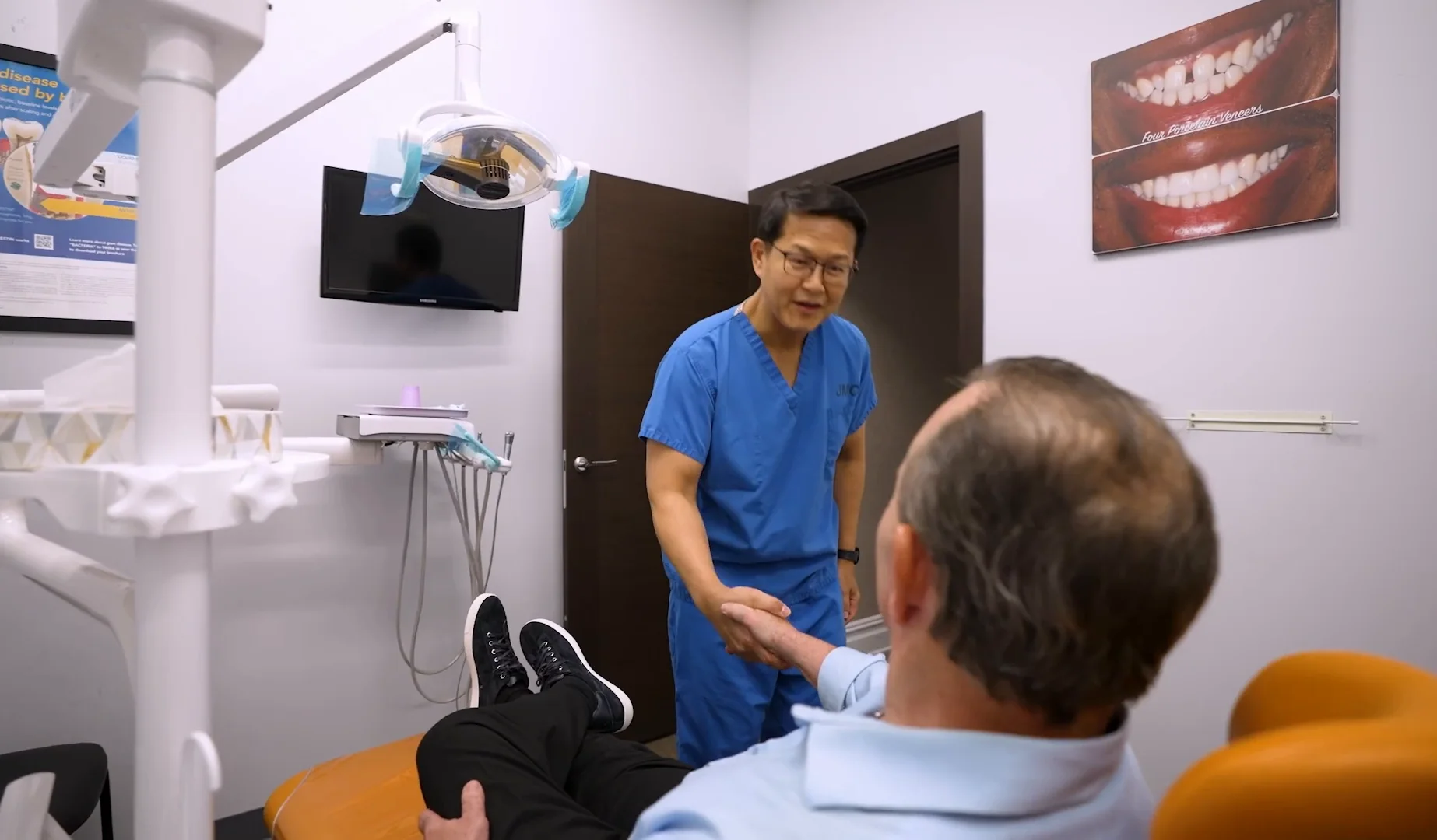 A patient reclined in a treatment chair, talking with a dentist