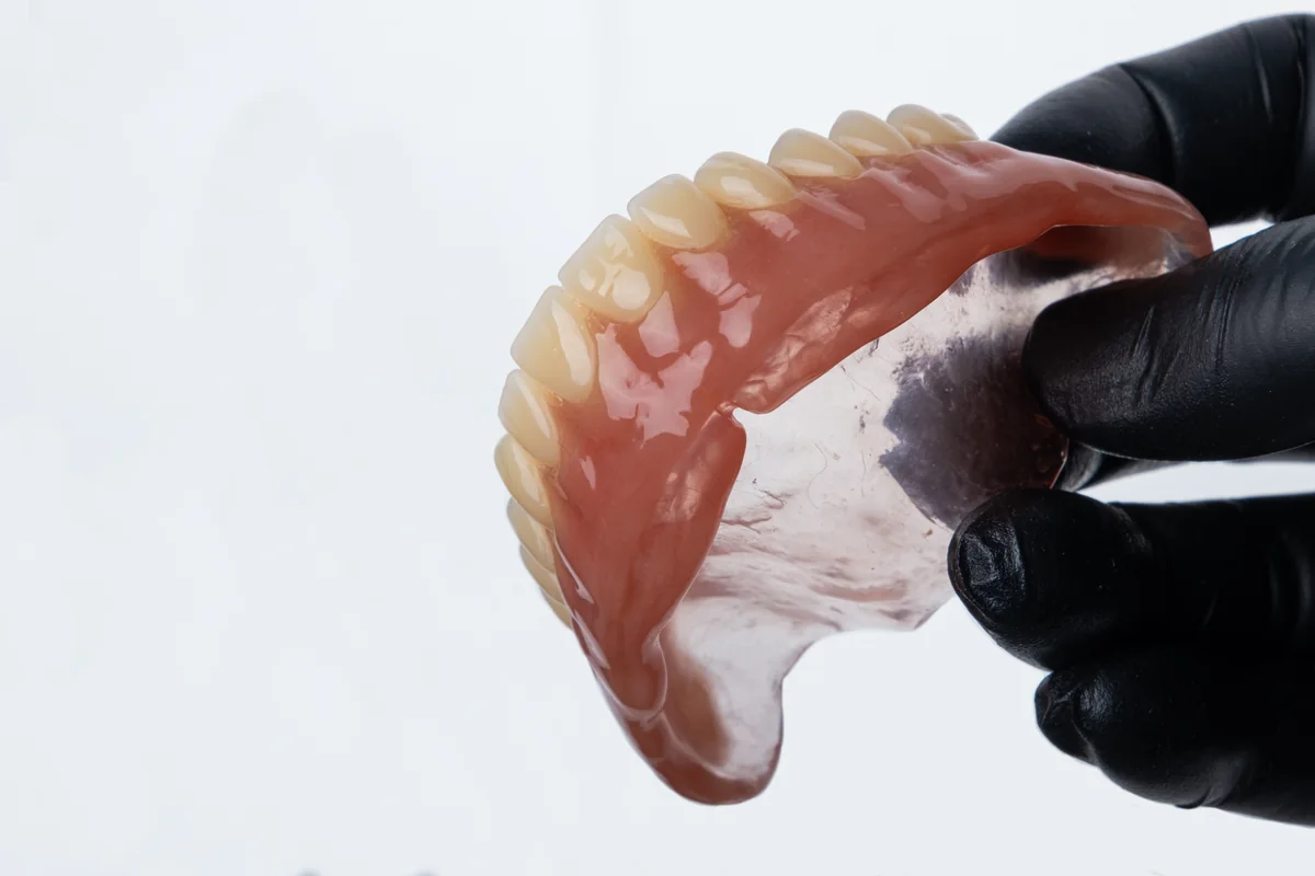 A full upper denture held in gloved hands