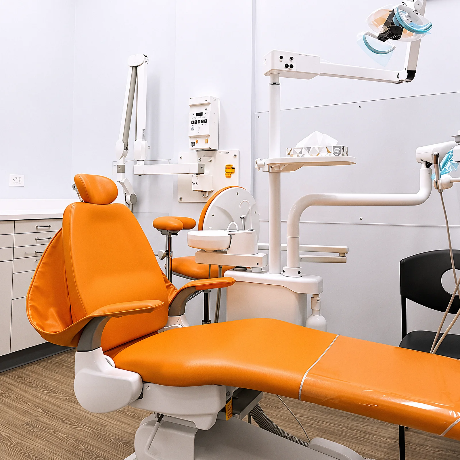 A treatment room with an orange dental chair under the light